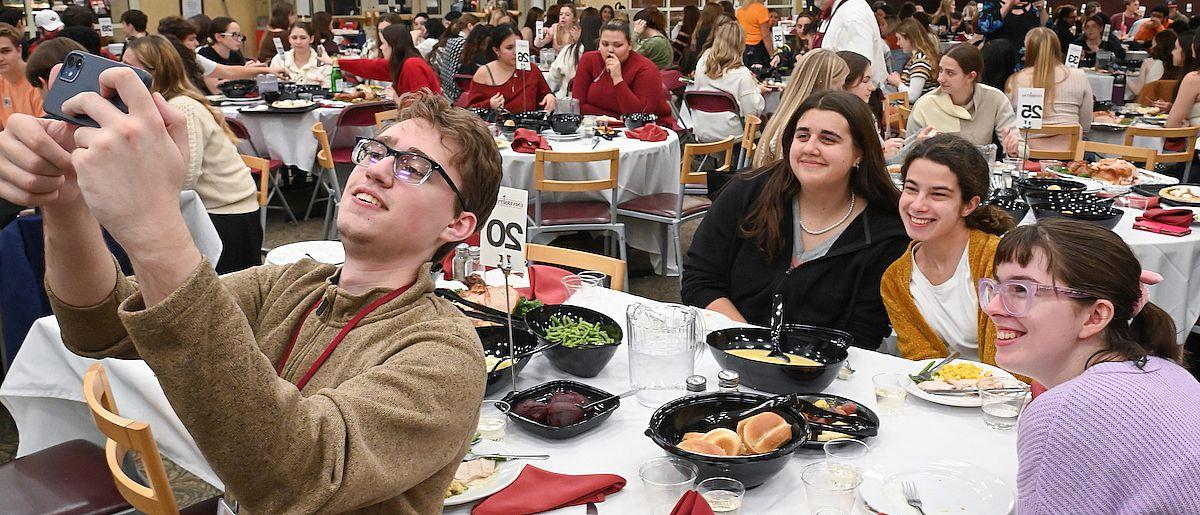 A student takes a selfie with the dinner participants in the background.