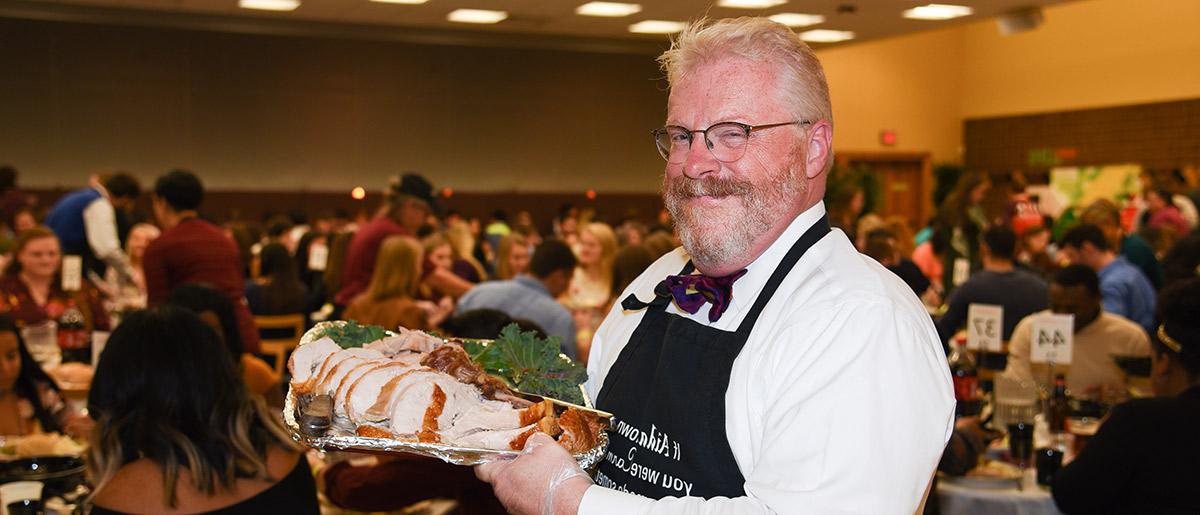 President Green smiles holding carved turkey at the Thanksgiving meal.
